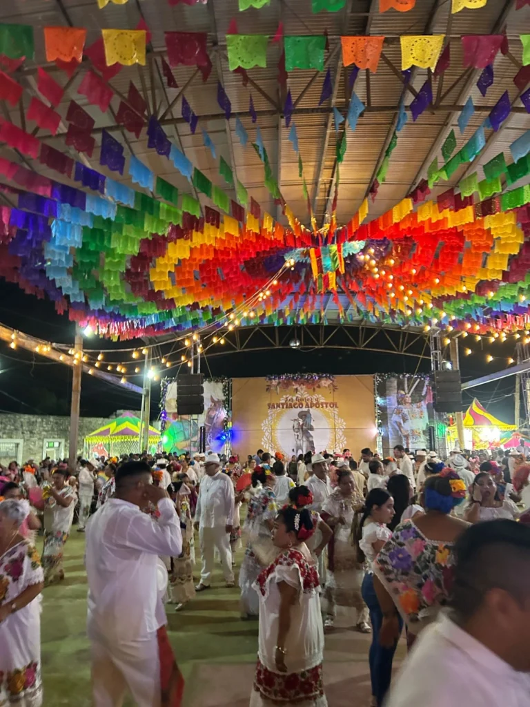 Personas con trajes típicos de Yucatán bailando en una fiesta tradicional bajo coloridas decoraciones de papel picado en Río Lagartos.
