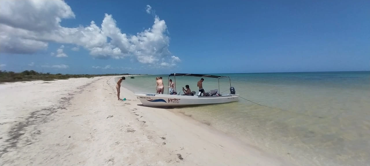 Rio Lagartos Beach: A Hidden Paradise of White Sand and Turquoise Waters in Yucatan 1 Pasajeros de nuestro tour en lancha tomando un descanso en una playa virgen de la Biósfera de Ría Lagartos, con el barco anclado en la orilla.