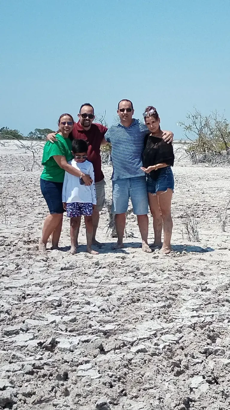 Happy family covered in clay, smiling and hugging during an authentic Mayan mud bath experience on a tour of the Las Coloradas pink lakes in Yucatan.