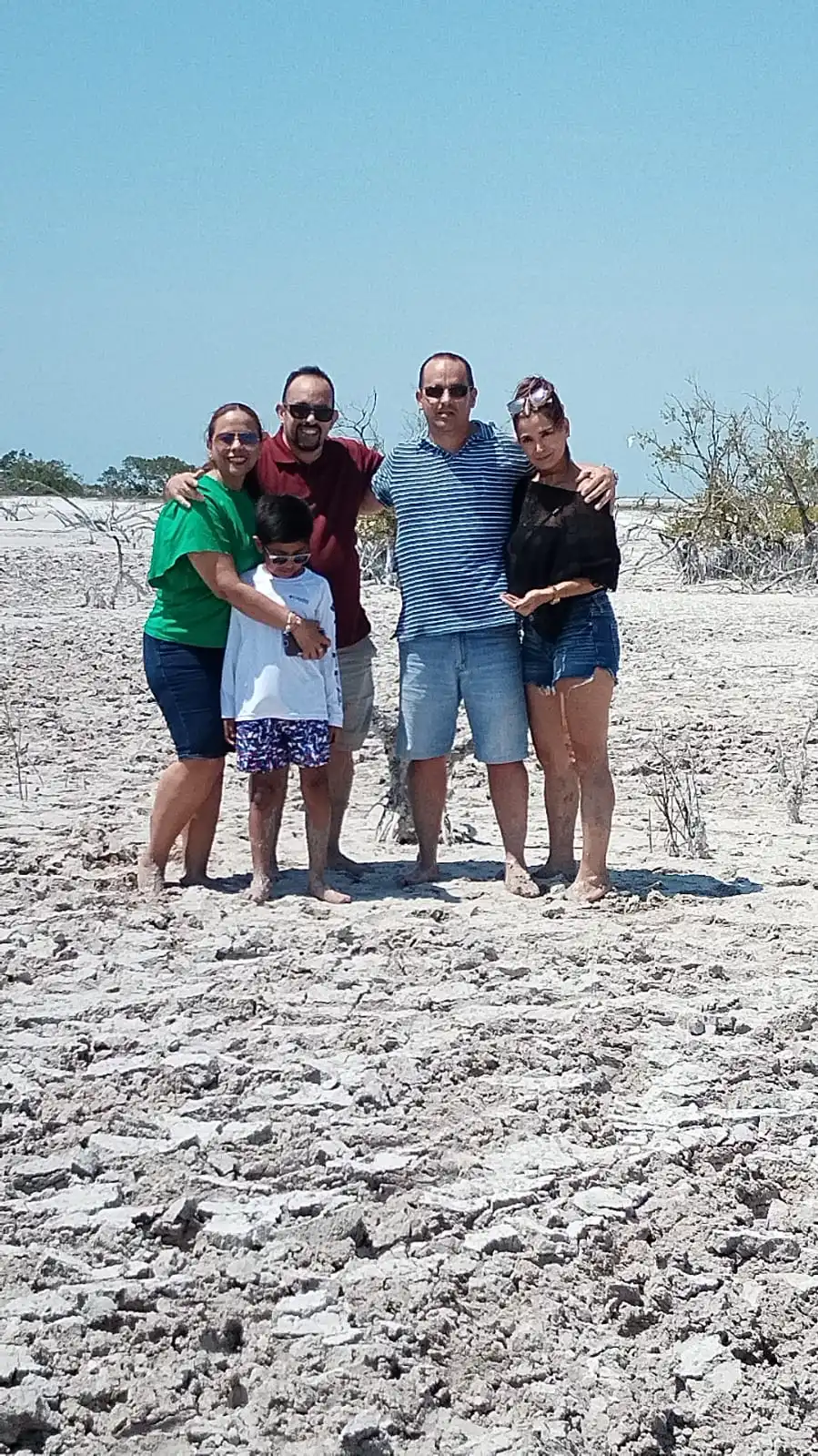 Happy family covered in clay, smiling and hugging during an authentic Mayan mud bath experience on a tour of the Las Coloradas pink lakes in Yucatan.