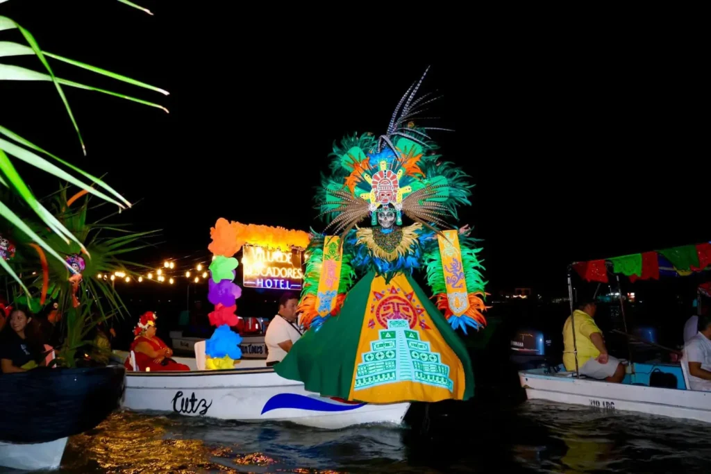 Una persona en una lancha durante el Paseo de Pixanes en Río Lagartos, luciendo un espectacular disfraz de inspiración maya con un gran penacho de plumas verdes y un faldón que representa una pirámide.