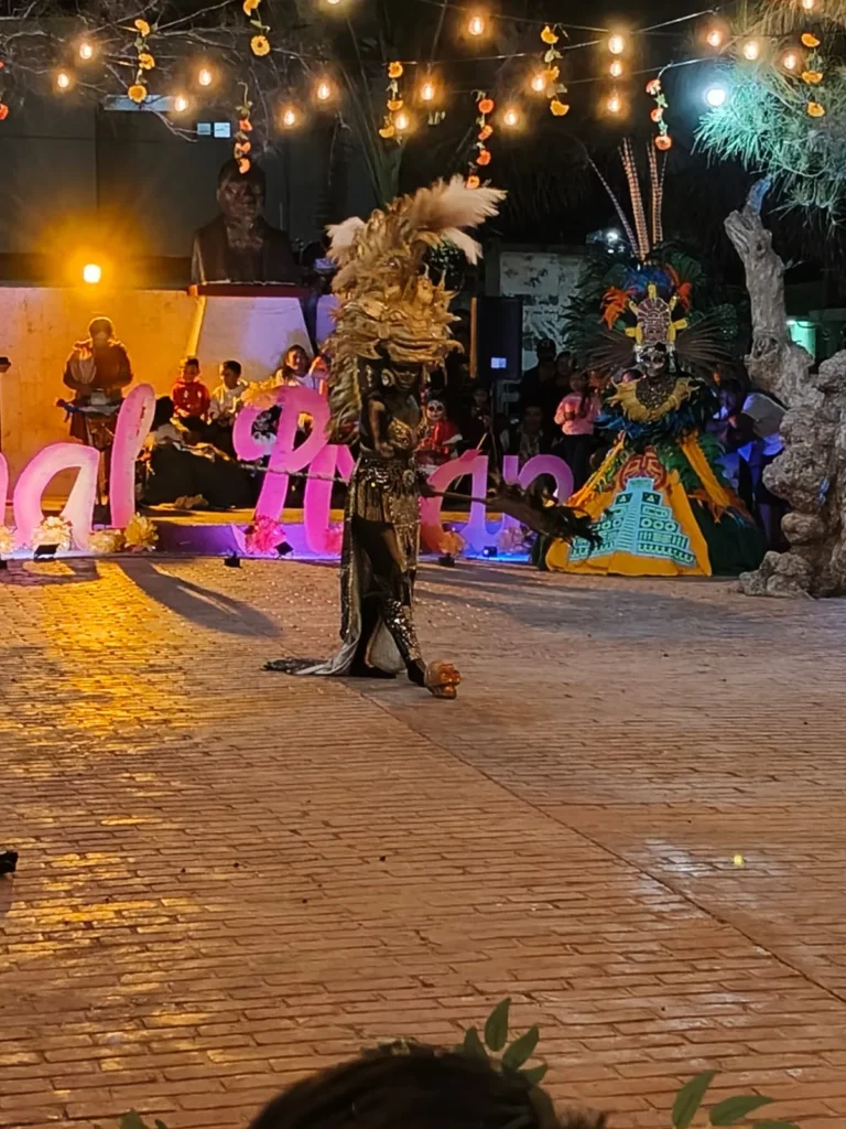 Danzantes con atuendos de inspiración maya realizando un ritual con fuego bajo luces de verbena durante el evento cultural del Festival de Ánimas en Río Lagartos.