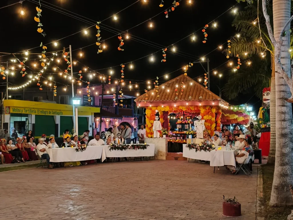Vista panorámica del evento cultural en el parque principal de Río Lagartos, con autoridades y el público sentados en mesas frente a un quiosco decorado como altar para el Festival de Ánimas.