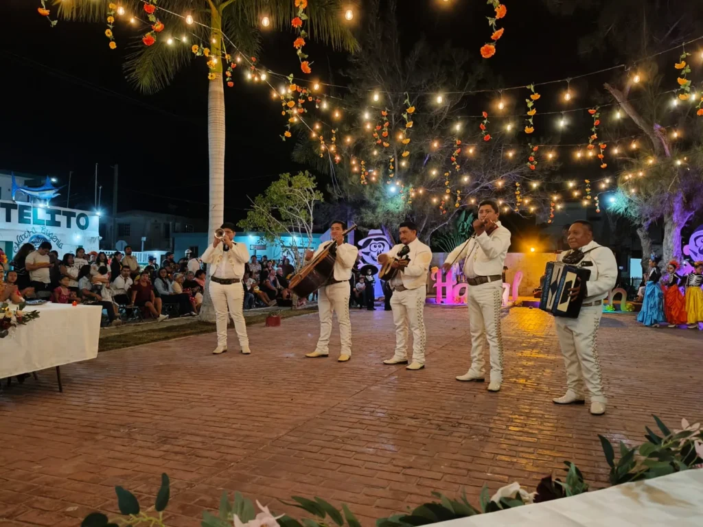 Un grupo de mariachis vestidos con trajes blancos tocando sus instrumentos en el parque de Río Lagartos, frente al público del evento cultural del Festival de Ánimas.