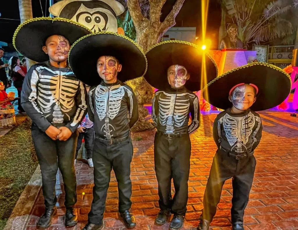 Cuatro niños pequeños disfrazados de catrines, con trajes de esqueleto y sombreros de charro, posando durante el Festival de Ánimas en Río Lagartos.