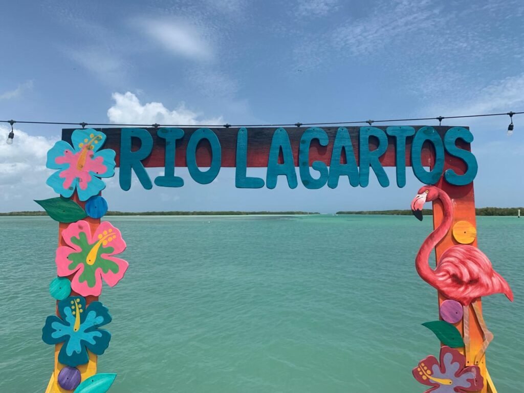 Vista de letras con las palabras de río lagartos y al fondo aparece parte de la salida hacia mar abiertoo, todo esto forma parte del itinerario tour río lagartos, los tours son privado en lancha por la Reserva de la Biosfera Ría Lagartos, incluyendo avistamiento de flamingos, Baño Maya y visita a Las Coloradas, Yucatán.