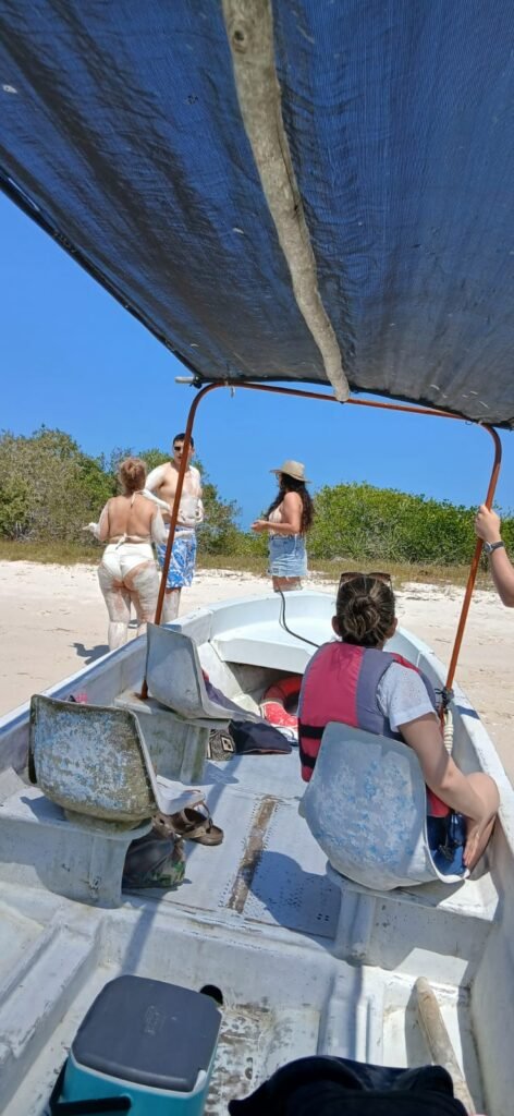 Tourists covered in white medicinal mud stand on a sunny beach next to their tour boat in Rio Lagartos, Yucatan, enjoying the Mayan Bath experience.